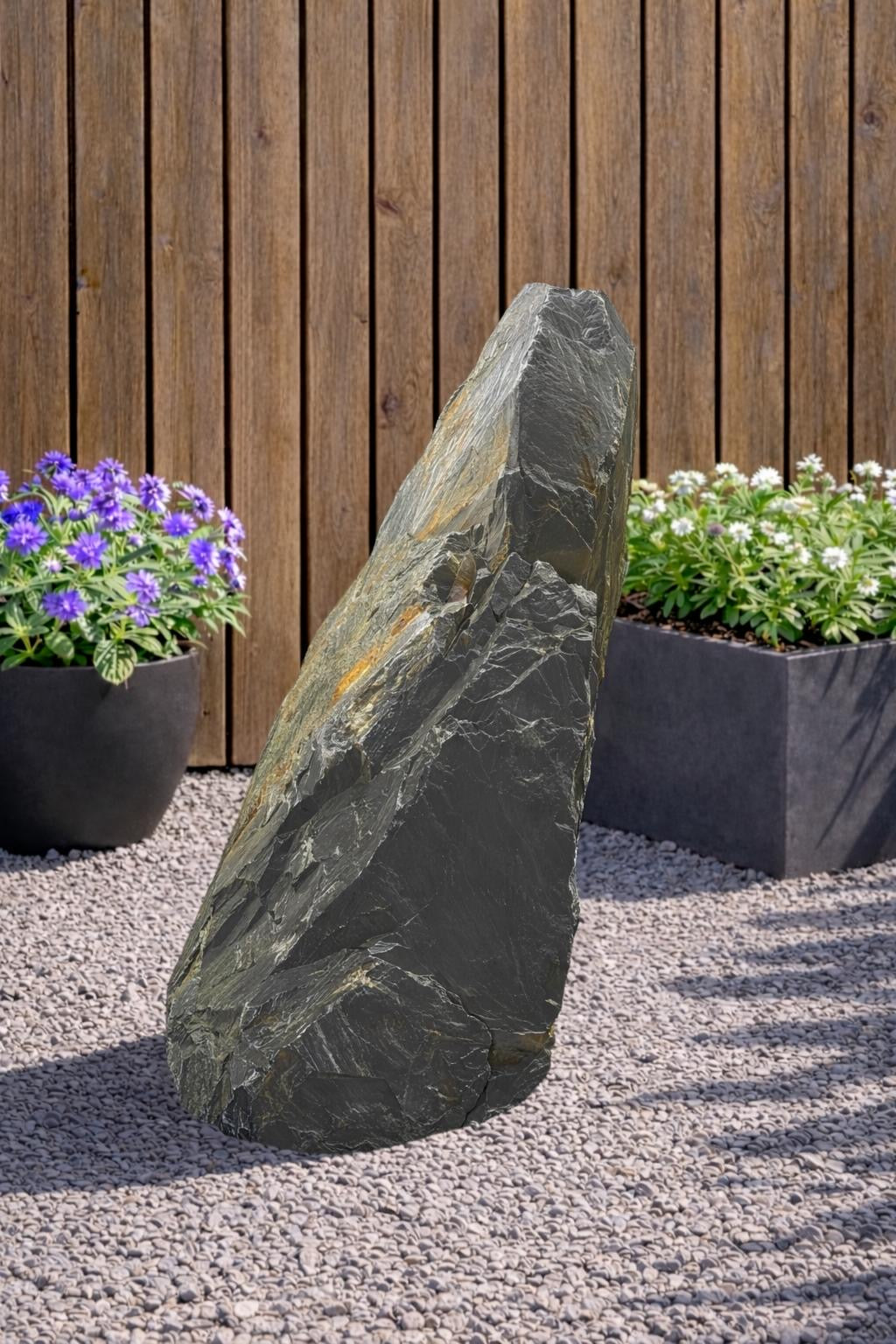 Grey slate monolith feature stone by Decorative Aggregates with natural stone texture, standing outdoors between plants.