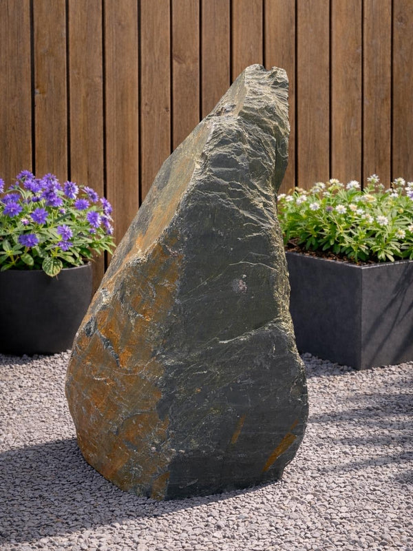 Slate monolith water feature, standing on gravel, with a rough, textured surface.