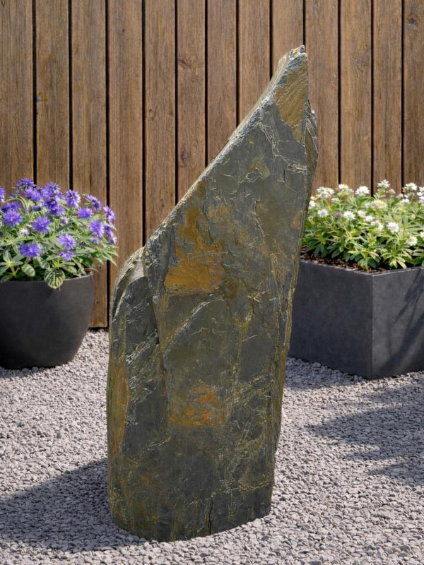 Slate monolith water feature from Water Feature 120 on a gravel surface with purple and white flowers.