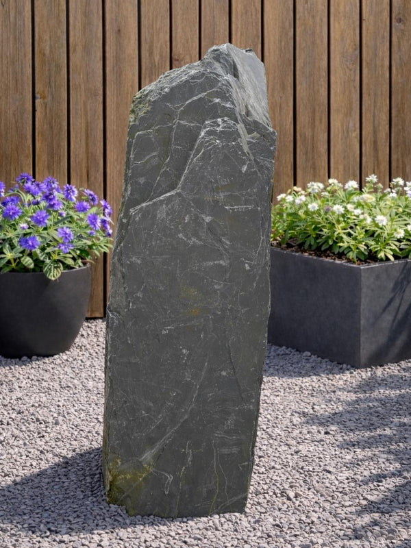 Gray slate monolith water feature from Water Feature with a rough, textured surface sitting on small gravel.