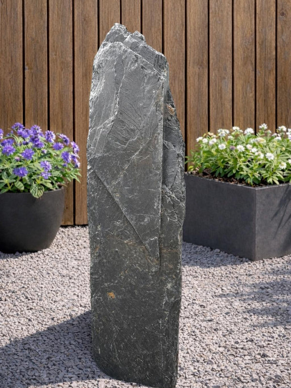 Slate monolith water feature by Water Feature 106, standing on gravel, with a rugged, layered texture.
