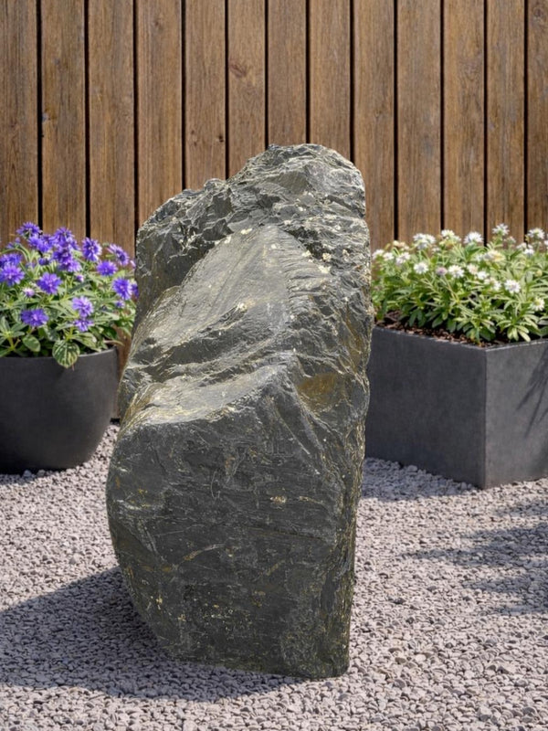 Grey slate monolith standing stone by 134, displayed outdoors with plants and gravel.