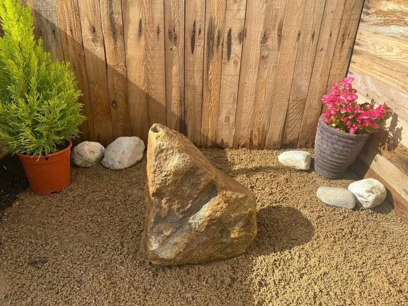 Natural drilled boulder water feature from BWF01, next to plants and smaller rocks on a bed of small stones.
