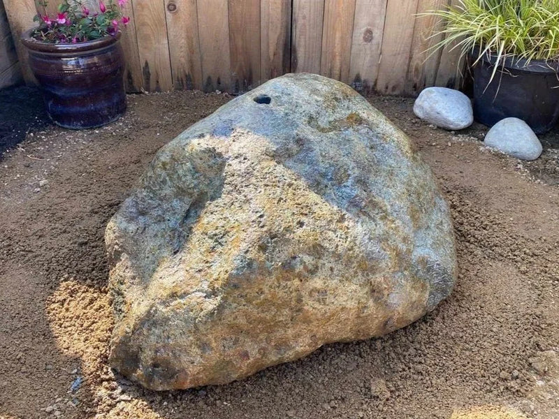 Natural drilled boulder water feature by EcoPonds, shown with earthy brown and blue colorations, rough texture, and a centered hole.