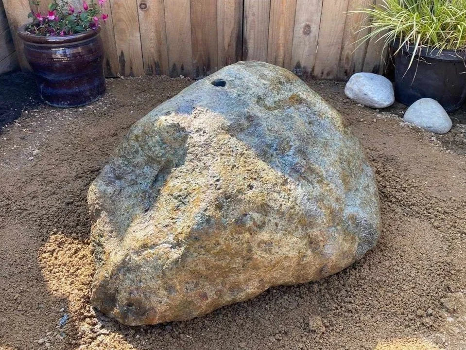 Natural drilled boulder water feature by EcoPonds, shown with earthy brown and blue colorations, rough texture, and a centered hole.