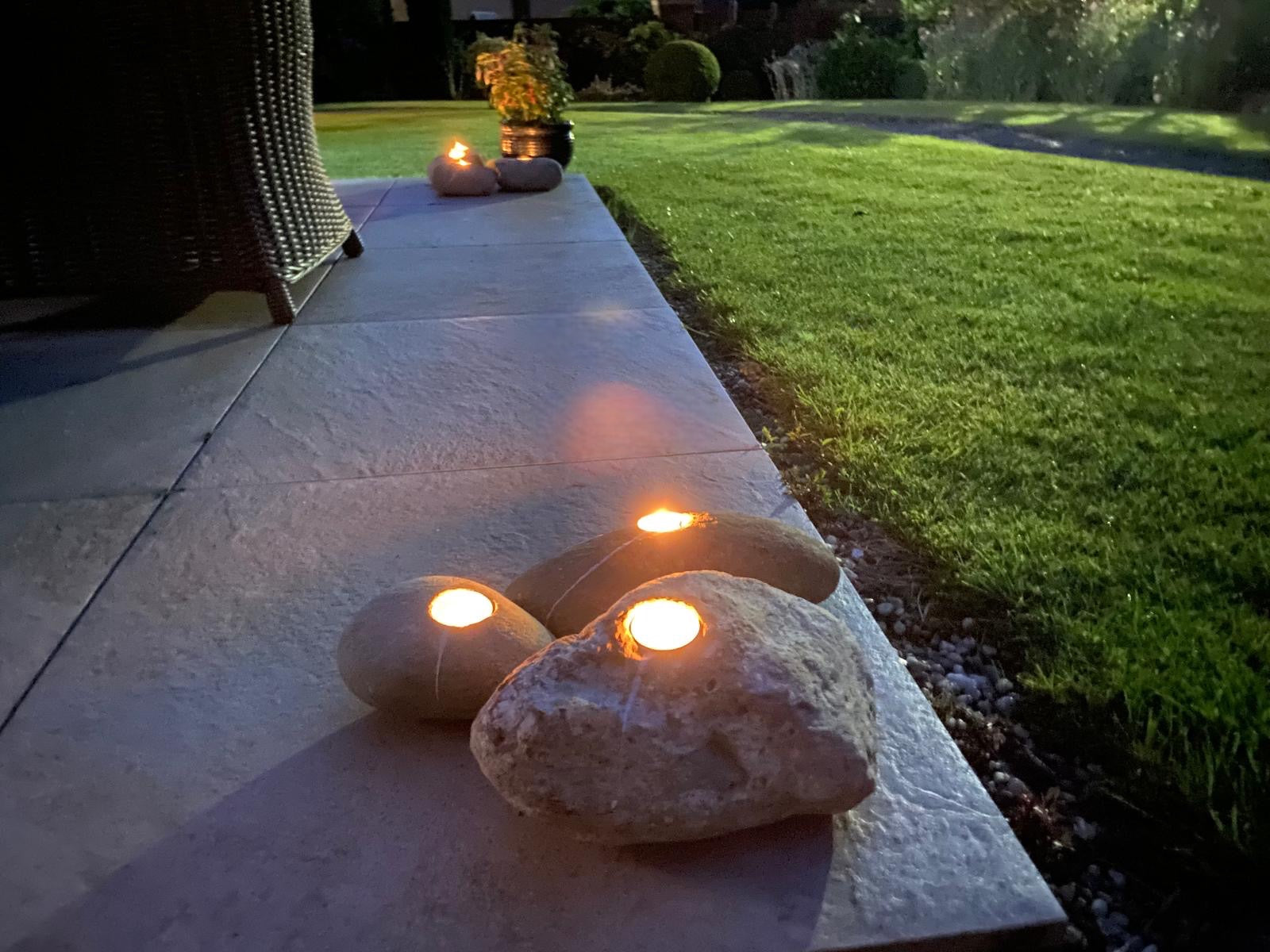 One-hole decorative candle stones with lit candles, on a patio and lawn, at night.