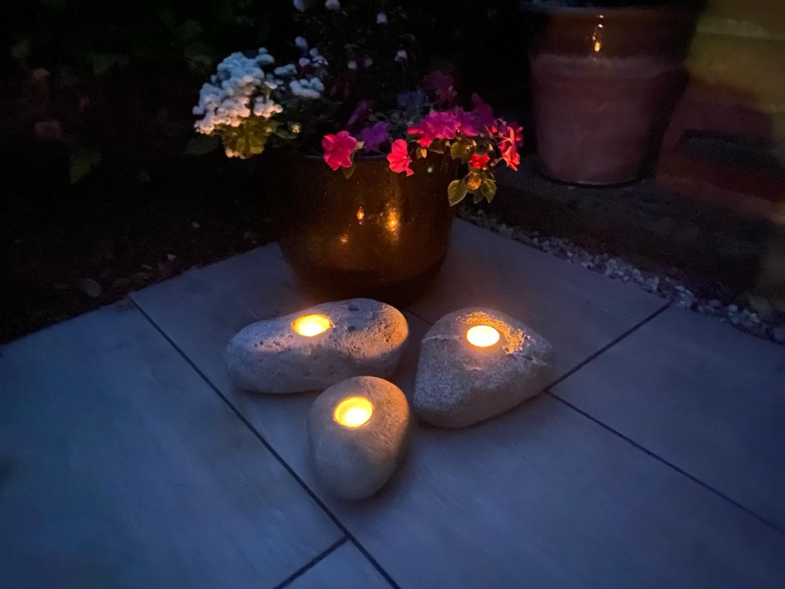 One-hole decorative candle stones with glowing tea lights, set on paving tiles near a flowerpot.