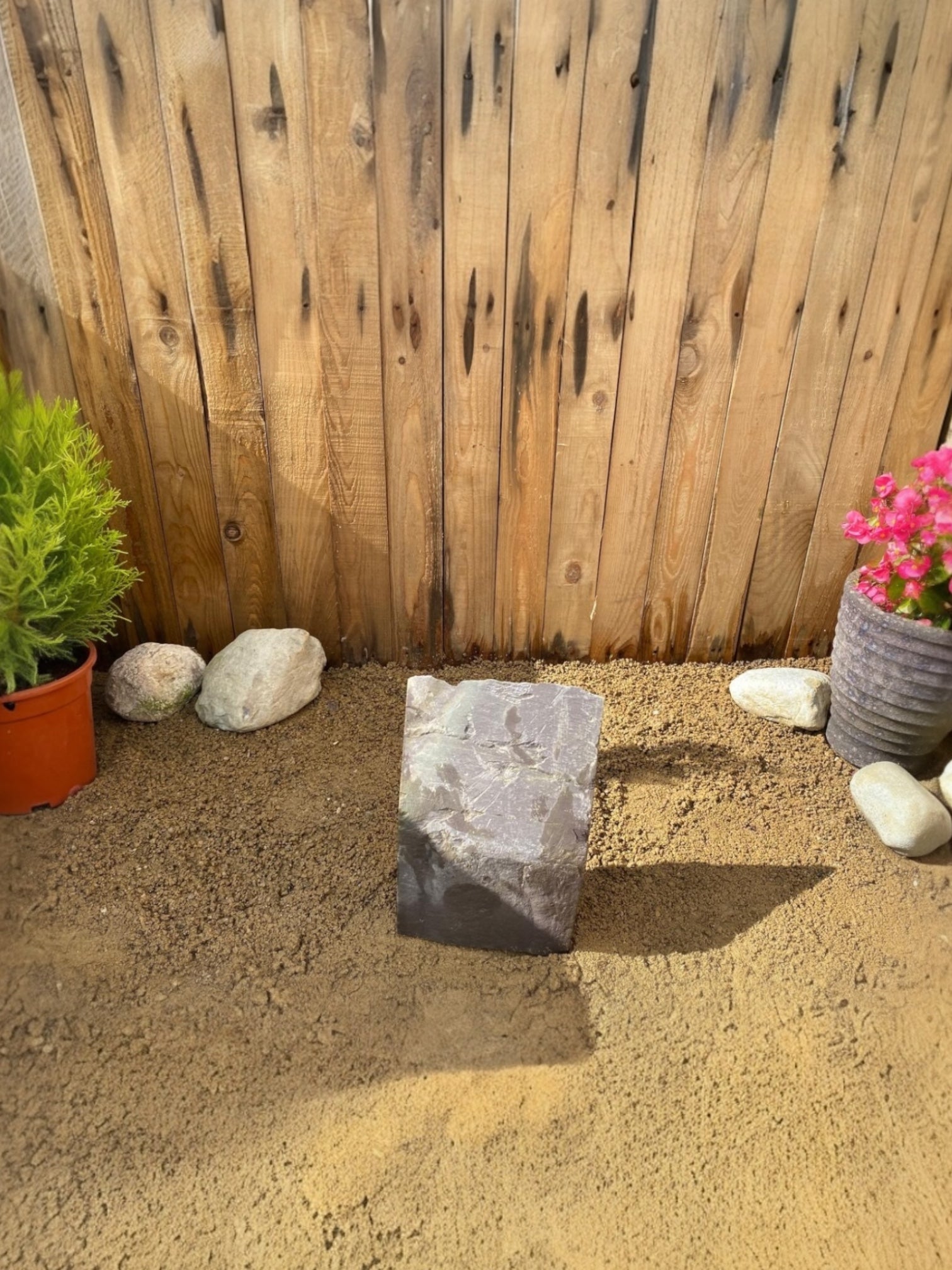Grey slate monolith by Water Feature PSM02, standing upright on gravel near other plants.