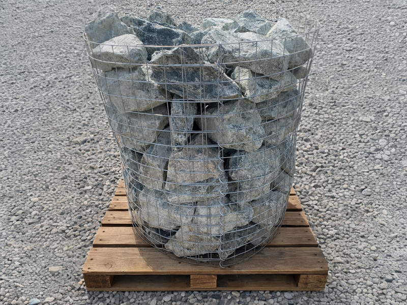 Green granite rockery stones by for gardens, contained in a metal wire basket on a wooden pallet.
