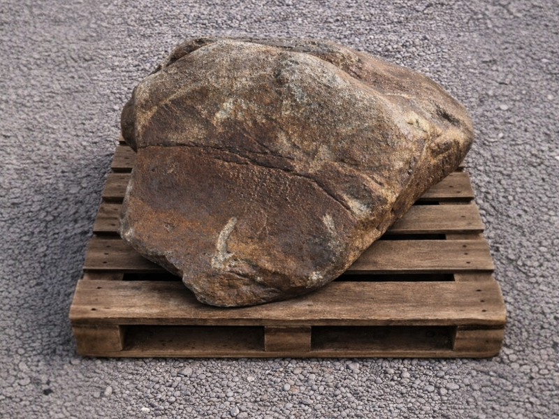 Extra large garden boulder with rough texture on a wooden pallet over gravel.
