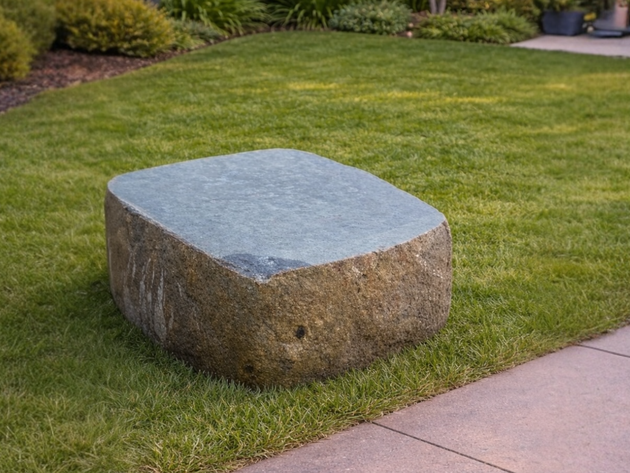 Sawn flat topped boulder seat for gardens with a smooth blue-gray top surface.
