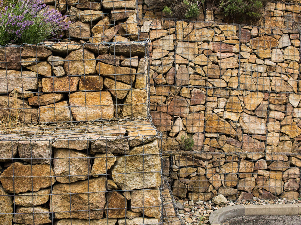 Golden granite gabion stones for gabion baskets, with wire mesh, stacked in a tiered retaining wall.