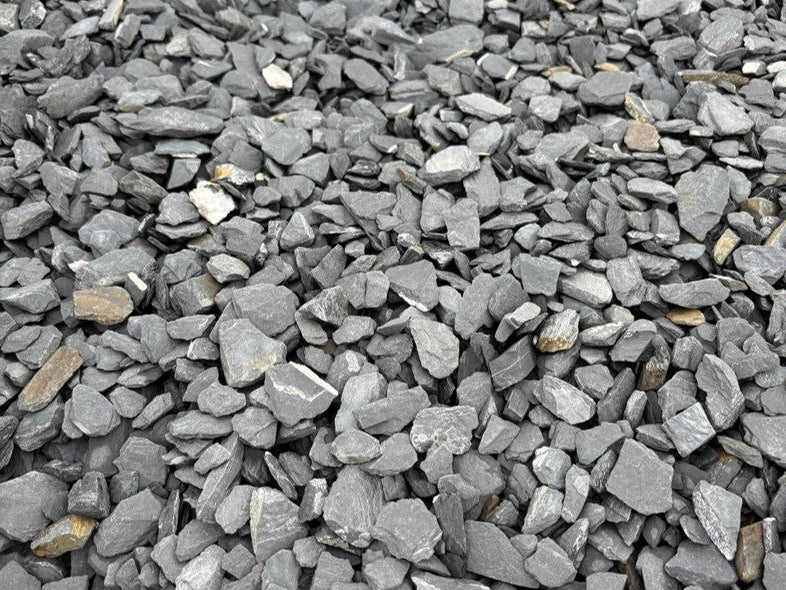 Grey slate mulch from a bulk bag, showing a rough, layered texture and varied fragment sizes.
