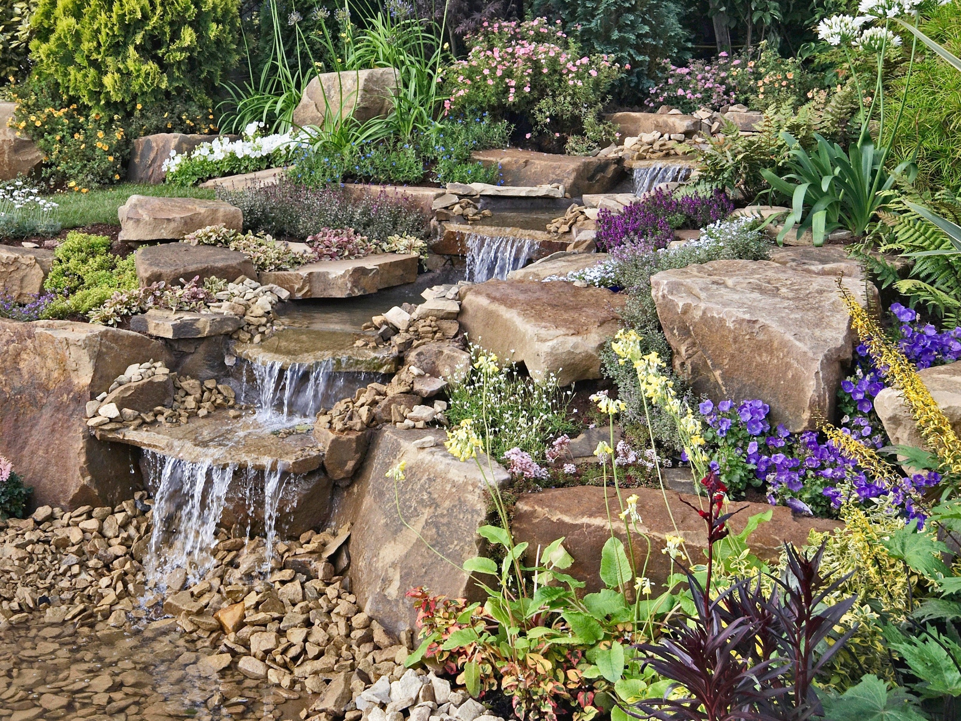 Natural golden granite decorative pond stones with water feature and colorful foliage.
