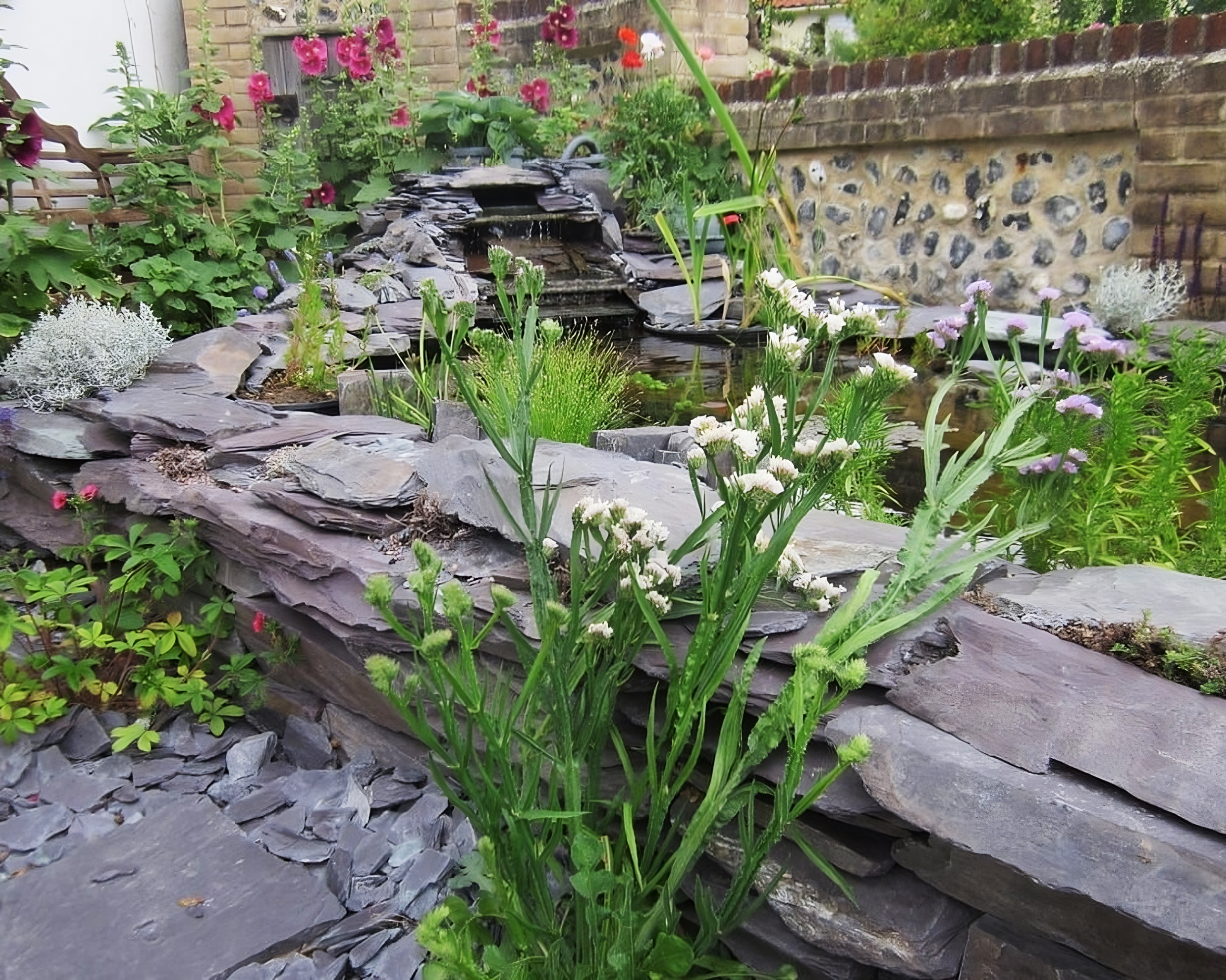 Decorative pond stones of plum slate with layering textures near a pond with foliage.
