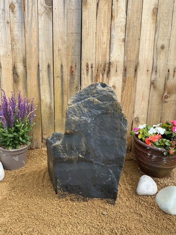 Slate monolith water feature, 600mm, with a natural dark grey texture, set among tan pebbles.