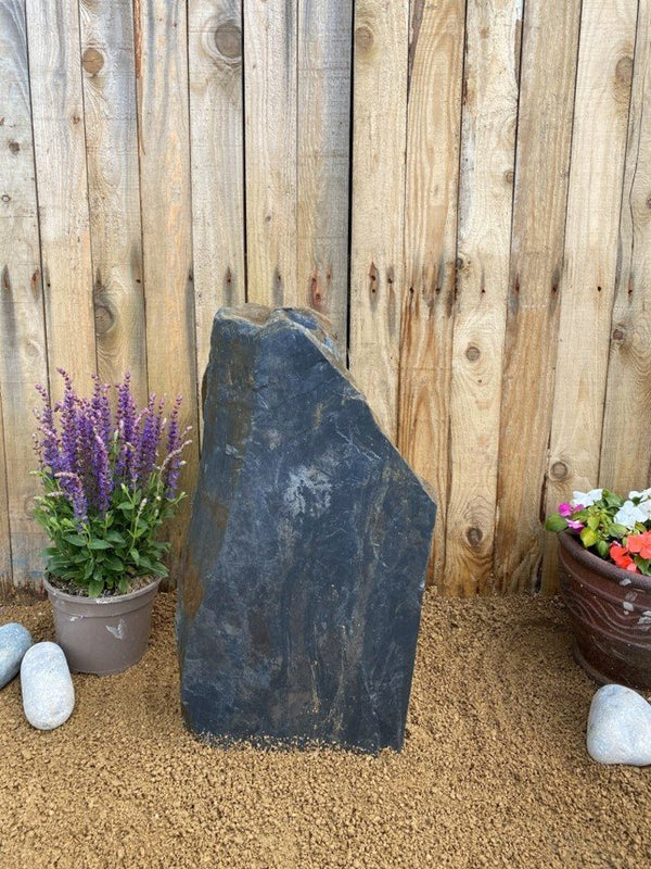 Dark grey slate monolith water feature from C011 standing outdoors near lavender and a wooden fence.