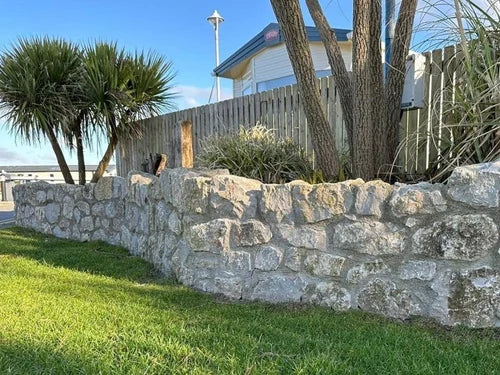 Natural limestone walling stone with varied texture against a backdrop of greenery.