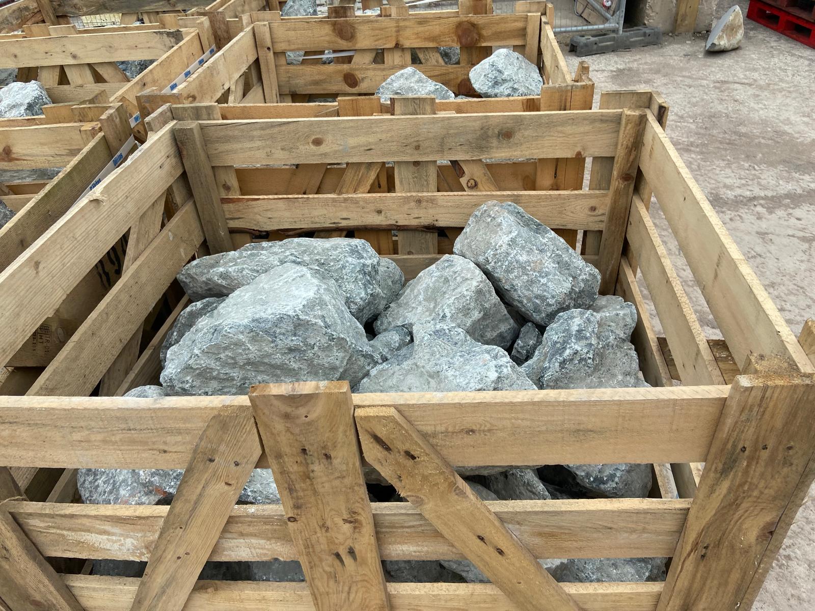 Natural green granite decorative pond stones, in wooden crates, no additional visual details.
