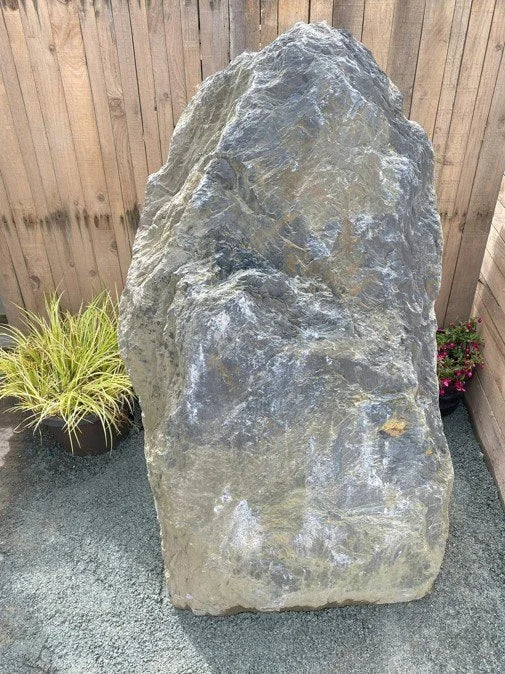 Grey slate monolith standing stone by Standing Stones, with a rugged texture, next to potted plants.