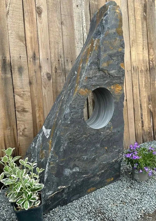 Hollolith grey slate water feature by an unspecified brand with a drilled hole, positioned near pebbles and plants.
