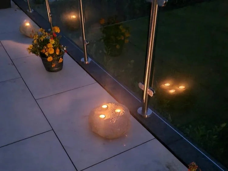 Three-hole decorative candle stones with embedded tea lights, illuminating a stone surface next to greenery.