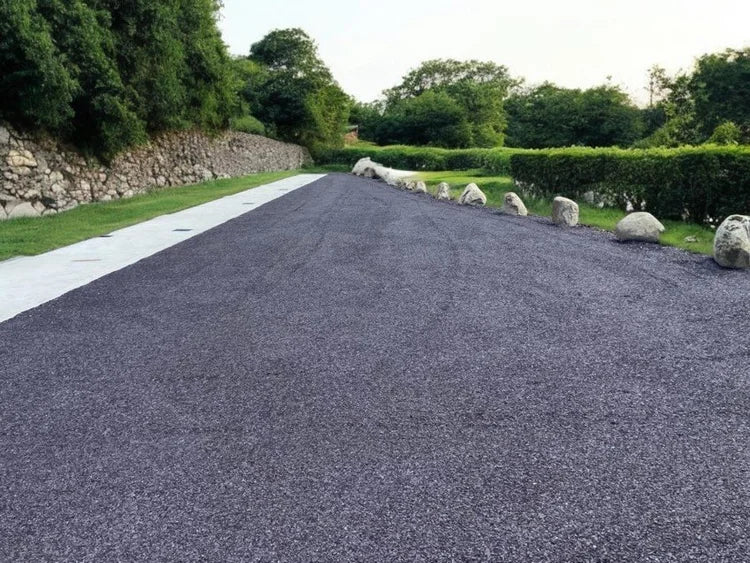 Plum slate self binding gravel for driveways, in a uniform texture, and laid alongside a retaining wall and green bushes.
