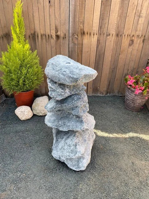 Small green granite water feature, 600mm, stacked on a gravel surface with plants in pots.
