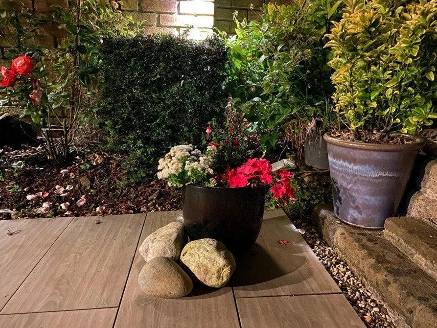 Natural glacial pond cobbles, 100-200mm, in varying light neutral tones, positioned on wooden pavers in an outdoor garden setting.
