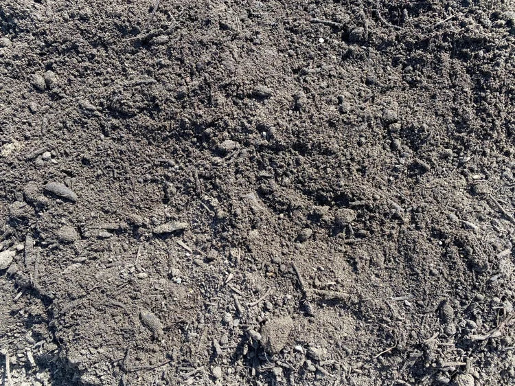 Dark top soil by bulk bag, featuring an earthy texture with small twigs and stones.
